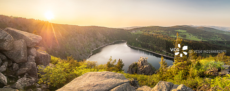 法国阿尔萨斯上莱茵省奥尔拜的著名自然地标——沃日山脉的白湖及其周边山脊的绝美全景，日落时分，地平线上有堆叠的岩石和落日。图片素材