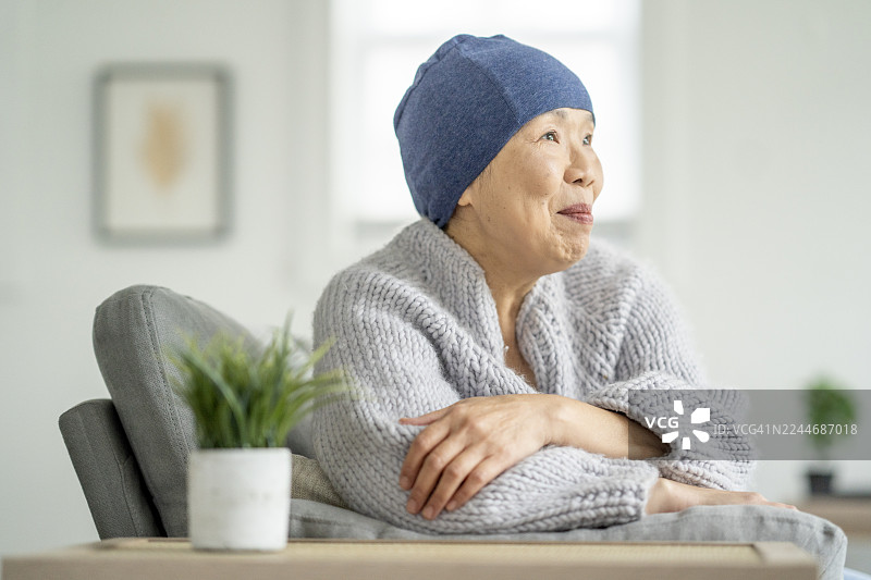 一位亚洲老年女性身穿舒适的针织毛衣在家中的沙发上放松图片素材