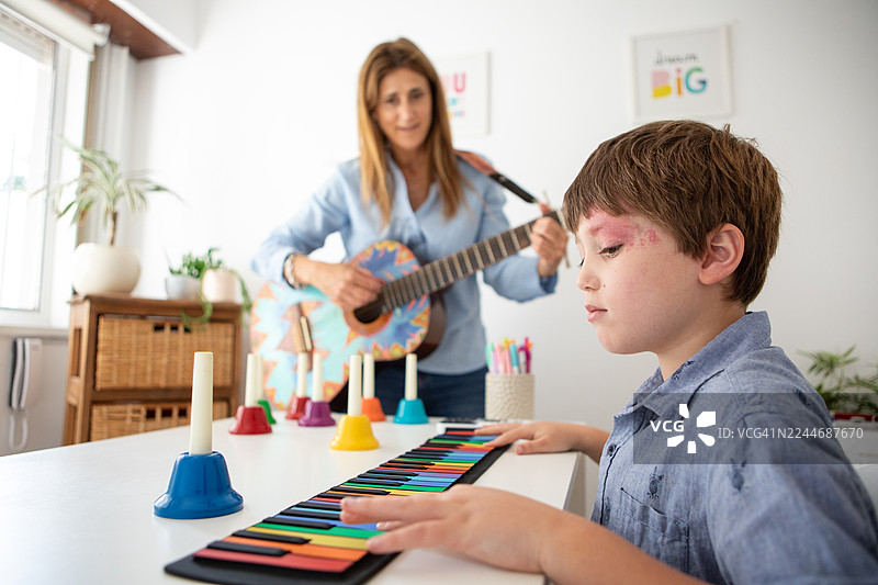 患有斯特奇-韦伯综合征的男孩在音乐治疗课上弹奏键盘图片素材