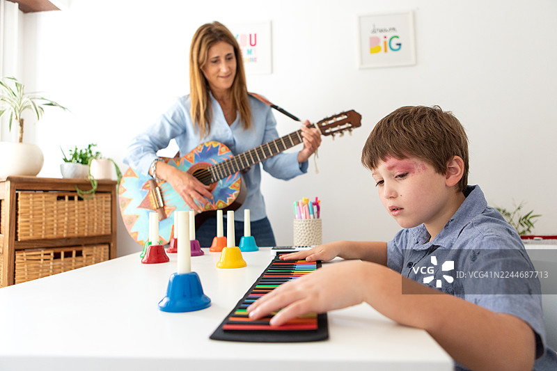 患有斯特奇-韦伯综合征的男孩在音乐治疗课上弹奏键盘图片素材