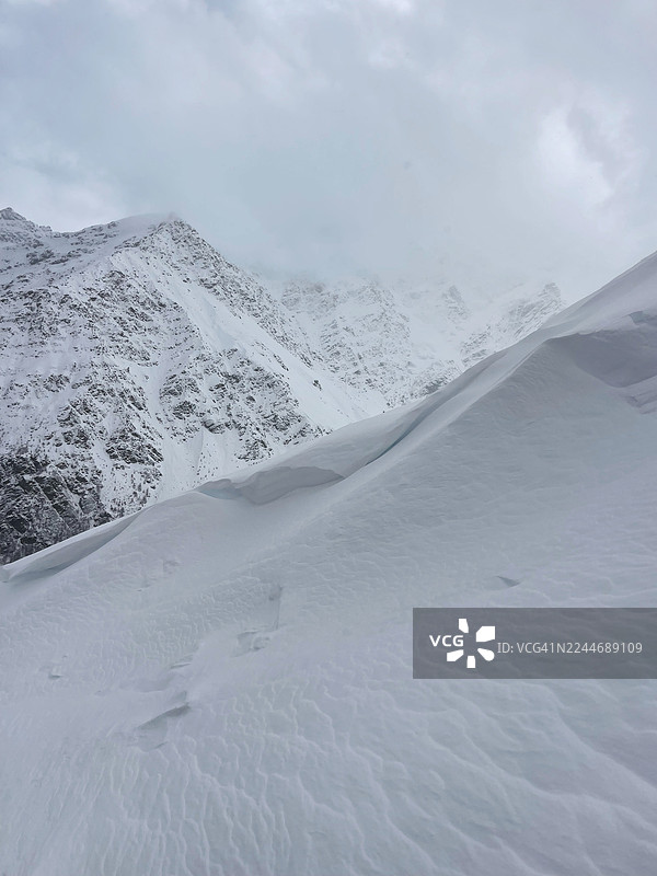 冬季荒野中，白雪皑皑的山脊在多云的天空下 â 广阔的雪原与崎岖的山峰图片素材