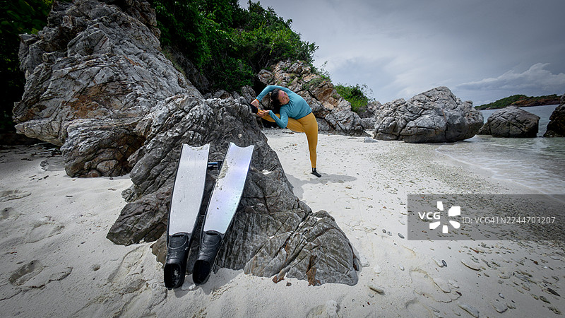 一名女子在热带海滩上练习瑜伽，背景是岩石峭壁，画面传达出放松、平衡与亲近自然的意境。图片素材