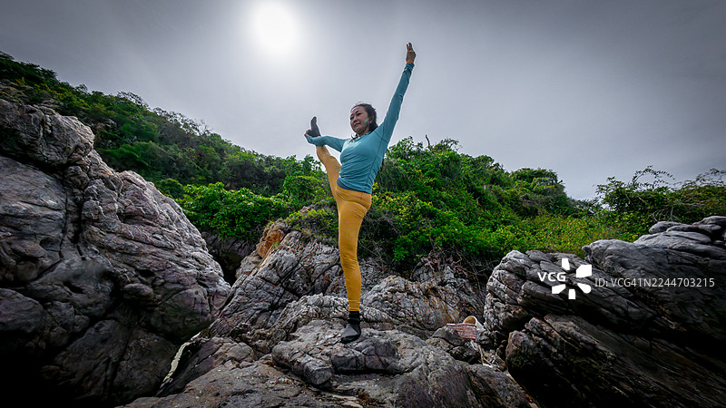 一位女性在热带海滩上练习瑜伽，背景是岩石悬崖，画面传达出放松、平衡与自然连接的意境。图片素材