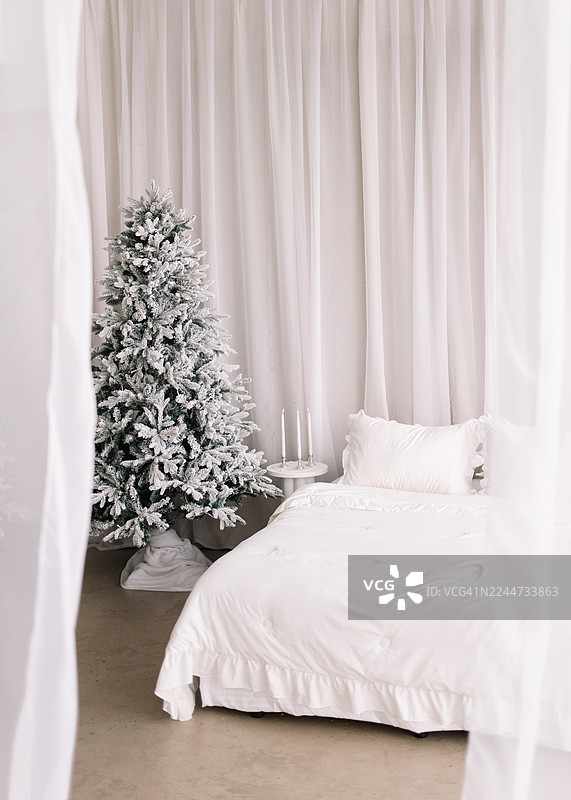 十二月冬日，卧室铺着白色床单的床，房间里装饰着圣诞树，充满节日气氛，温馨的季节性室内概念图片素材