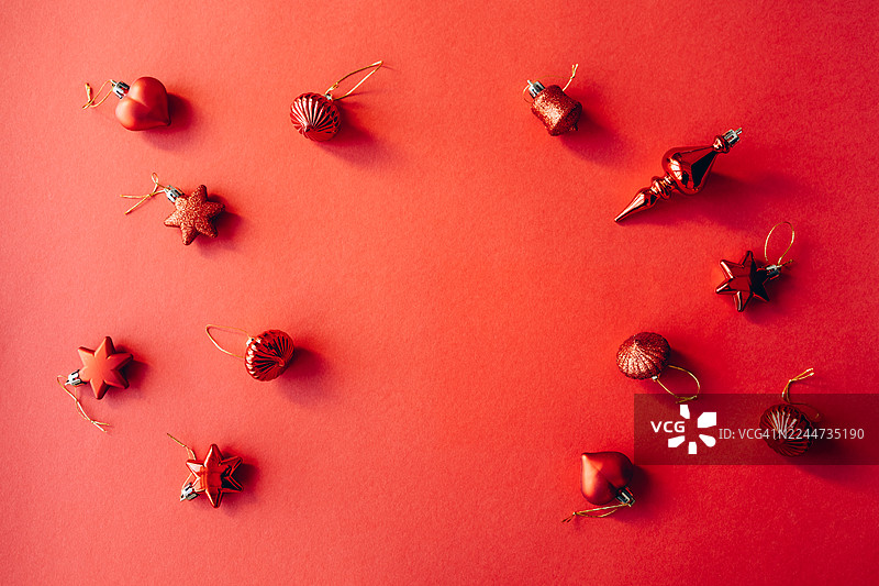 红色背景上，各种红色圣诞装饰球、星星和节日装饰品平铺排列，中心留空。图片素材