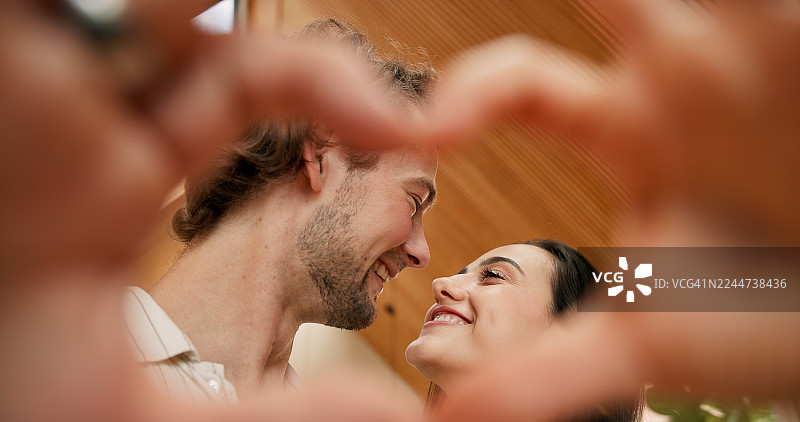 一对情侣和一群人做出心形手势，象征着对爱人爱、浪漫和亲情。男女开怀大笑，用手指做出承诺、关爱和伴侣关系的手势，背景是房子。图片素材