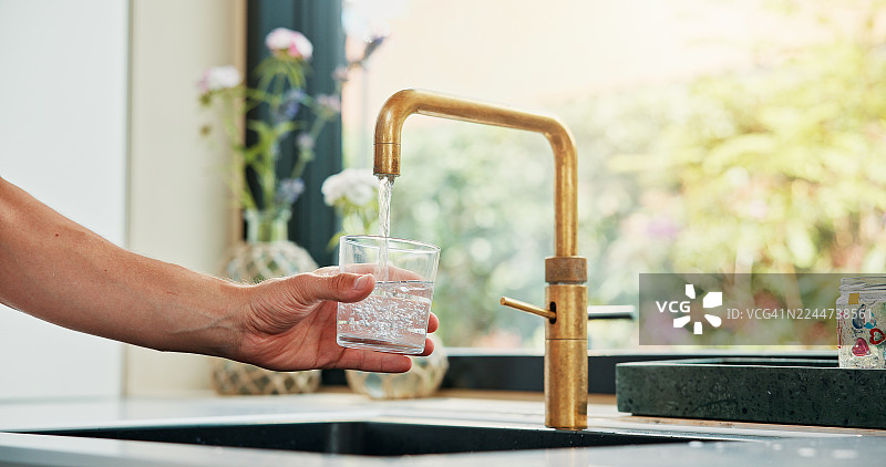 早晨在家中，手、玻璃杯和水龙头象征着补水、健康和排毒的自我护理。在公寓的厨房里，一个人拿着水龙头和水，为了喝水、解渴或补充电解质以促进肠道健康。图片素材
