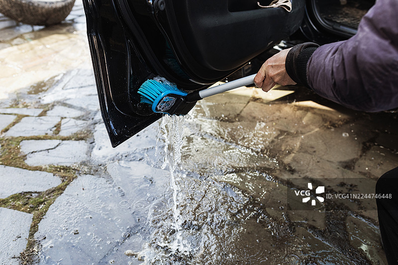 一个人正在户外用蓝色刷子和喷水器清洗汽车车门图片素材