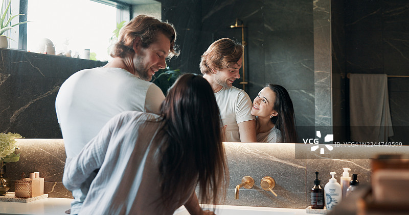 一对情侣在家里的浴室里，在早晨的护肤例程中，充满爱意地依偎在一起，脸上洋溢着幸福的笑容。周末，这位女士在镜子前拥抱着她的伴侣，进行着皮肤护理，彼此间充满了温情。图片素材