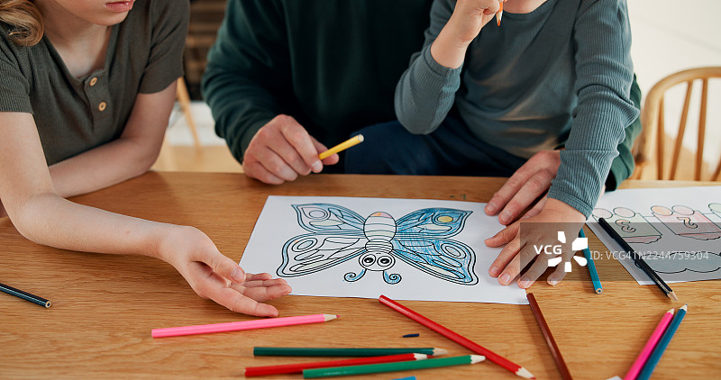 在家中，孩子的双手在桌前进行艺术家庭作业，得到支持、帮助和学习。这是一个家庭项目，孩子们用彩色铅笔进行创作，家人一起度过亲子时光，促进儿童发展。图片素材
