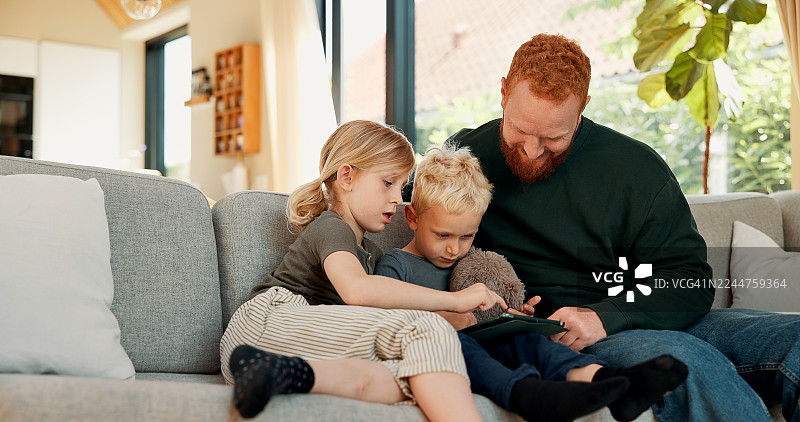 一家人，包括爸爸和孩子们，在沙发上一起玩平板电脑上的网络游戏、观看卡通视频并享受亲子时光。放松、居家，男人与孩子们一起使用数码科技，在客厅里上网、看电影、增进感情。图片素材