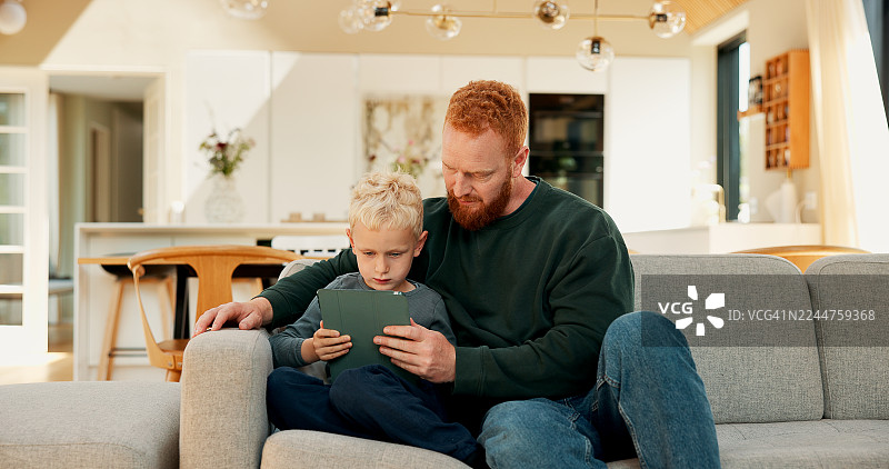 远程教育，爸爸和孩子一起使用平板电脑，在家阅读电子书，培养数字素养，增进亲子关系和共同成长。网络在线教育，父子在家中学习知识，通过科技和网络故事实现成长与发展。图片素材