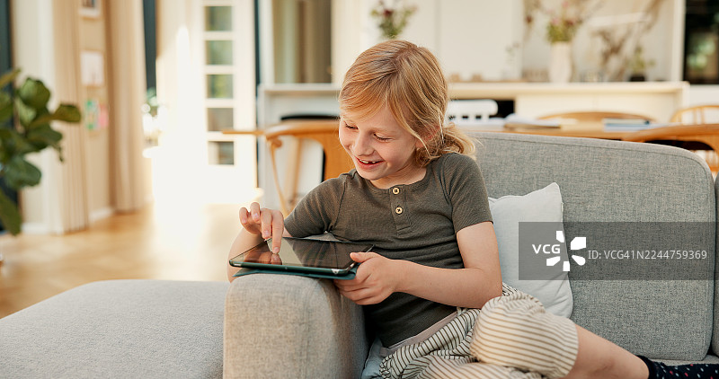 放松、快乐的孩子在沙发上使用平板电脑玩教育游戏、在线观看视频和使用电子学习应用。在家中，女孩微笑着使用数字技术观看视频、上网和连接，身处客厅。图片素材