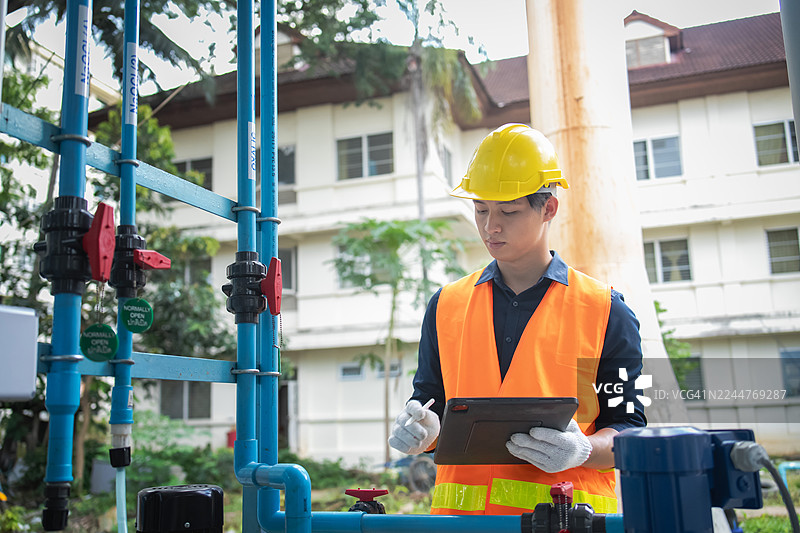 技术人员在工业环境中，使用平板电脑检查控制面板，确保设备正常运行。图片素材