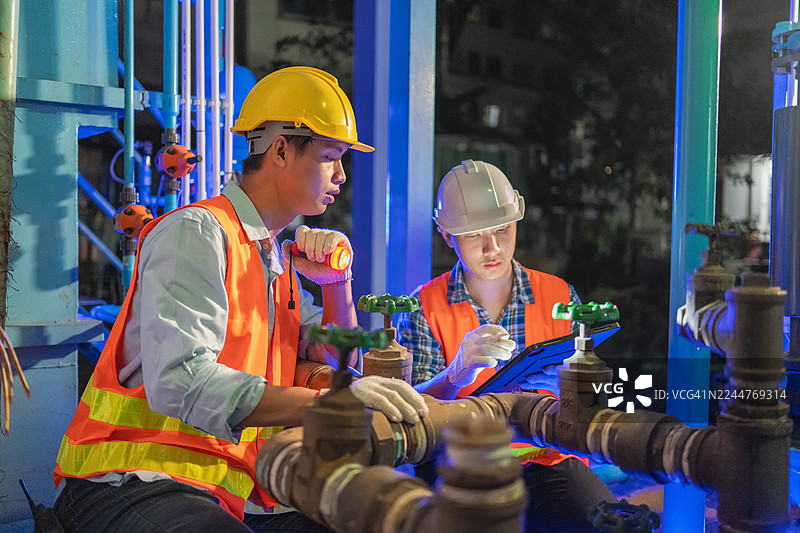 勤奋的工人在光线昏暗的工厂里检查工业管道，确保生产运营的维护和安全。图片素材