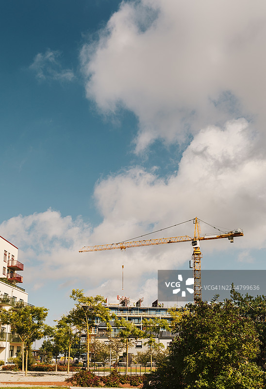 背景为多云天空的房屋建筑剪影，前景是建筑起重机。图片素材