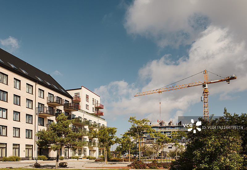 房屋建筑上方建筑起重机的剪影，背景为多云的天空。图片素材