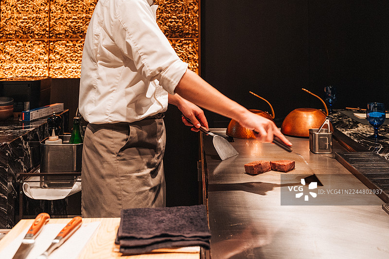 大厨在铁板烧烤架上为客人烹饪优质牛排。图片素材