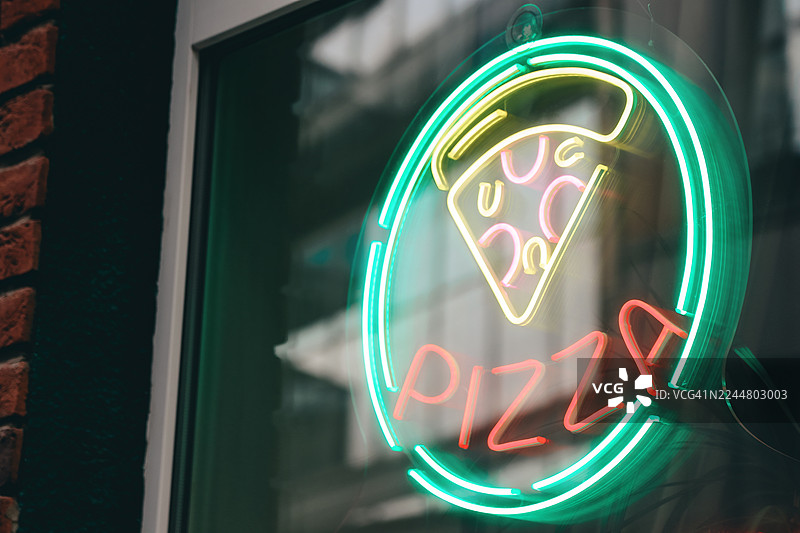 背景是当地人行道披萨店，霓虹灯招牌色彩鲜艳，上面有一片披萨图片素材