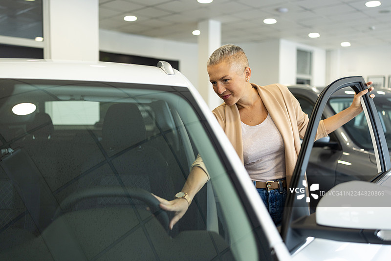 一位女士在现代展厅里选购汽车，正在检查一辆白色SUV。图片素材