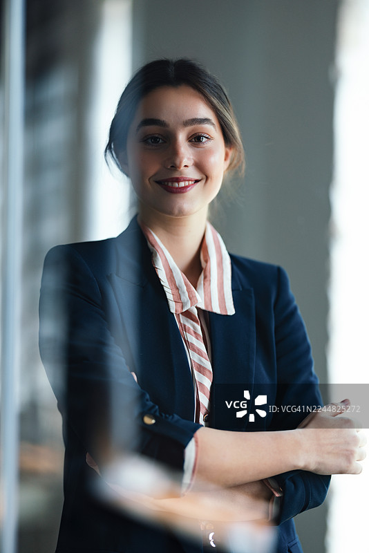 自信的商界女性身穿海军蓝西装外套，在现代办公室环境中微笑，专业肖像照图片素材