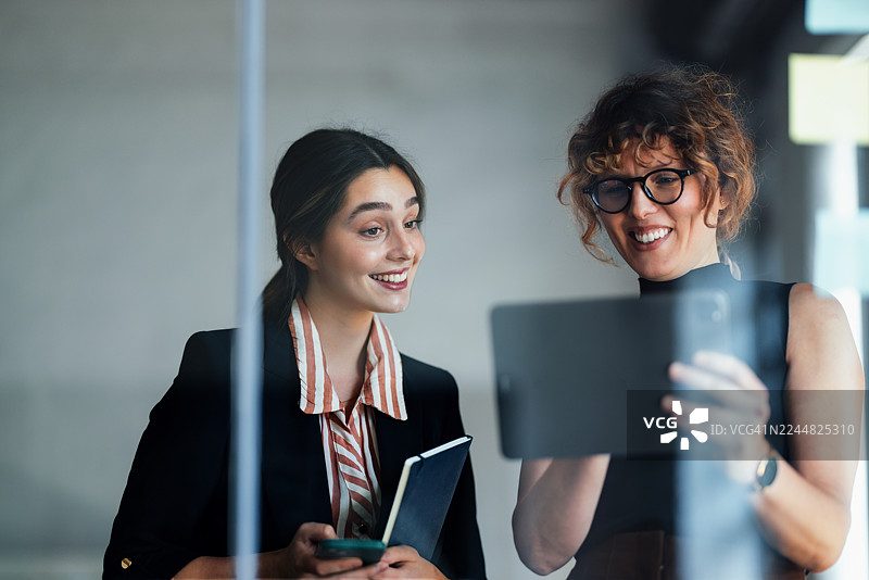 现代办公室里，专业女性使用平板电脑和智能手机协作图片素材