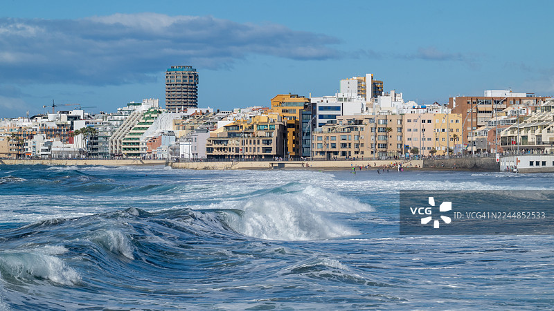 海浪拍打在拉斯帕尔马斯德大加那利岛天际线前的沙滩上图片素材
