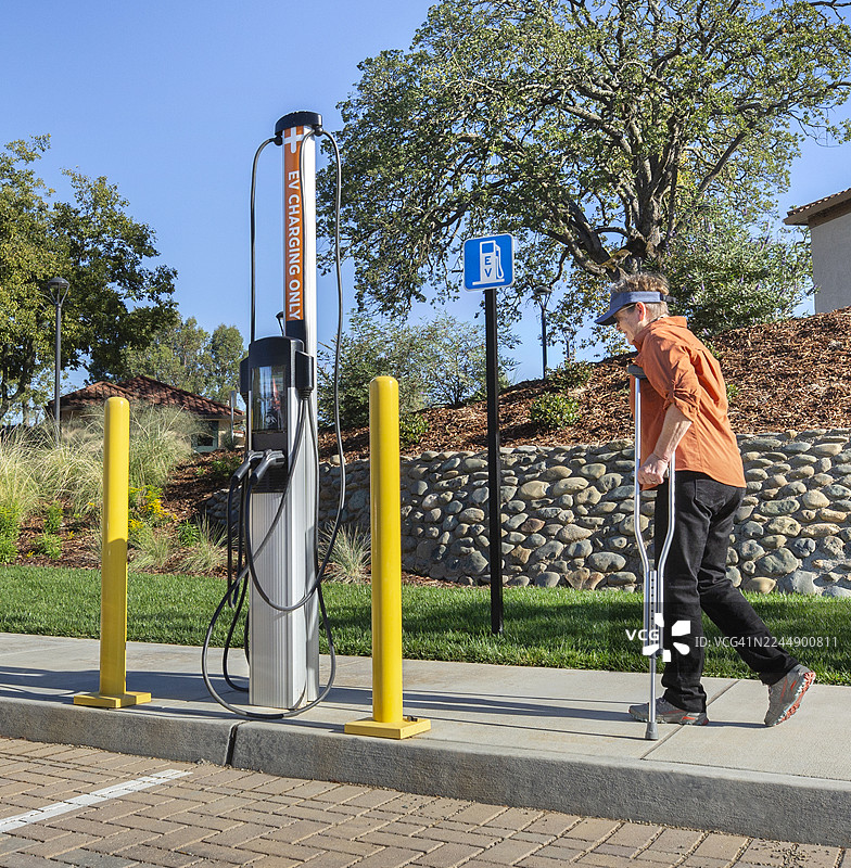 一名残疾成年女性，拄着拐杖，在电动汽车充电站附近行走图片素材