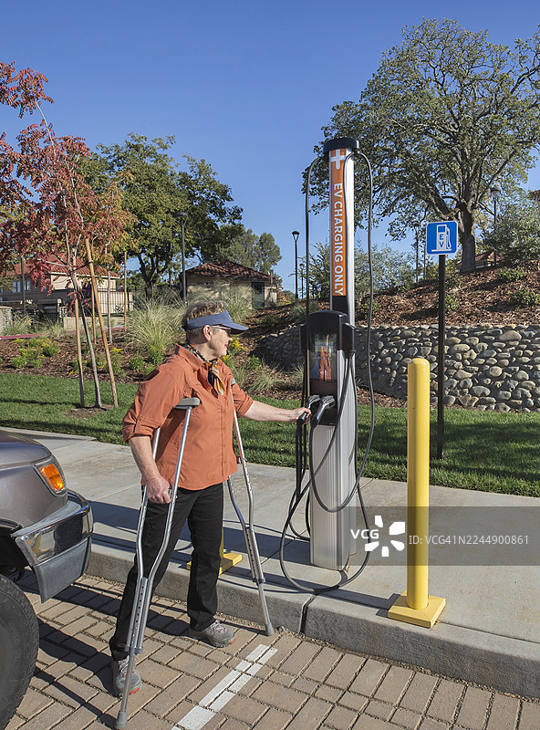 一名残疾成年女性，拄着拐杖，站在电动汽车充电站旁边图片素材