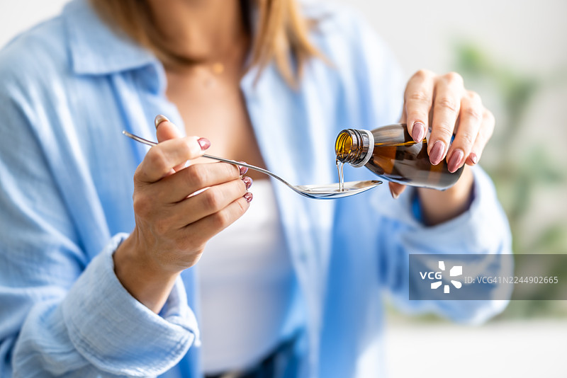 特写镜头，一位女性的手将糖浆倒在勺子上，用于治疗有痰或干咳。图片素材