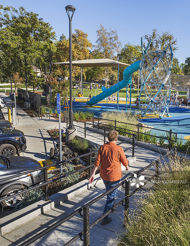 一位年长女性在公园里悠闲地走在水泥斜坡上，旁边是草地区。图片素材