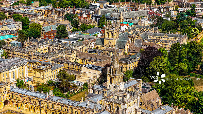 牛津历史悠久的大学学院的鸟瞰图，拥有哥特式塔楼和石头尖顶，标志性的学术建筑被绿植和城市屋顶环绕，文化遗产与教育理念图片素材