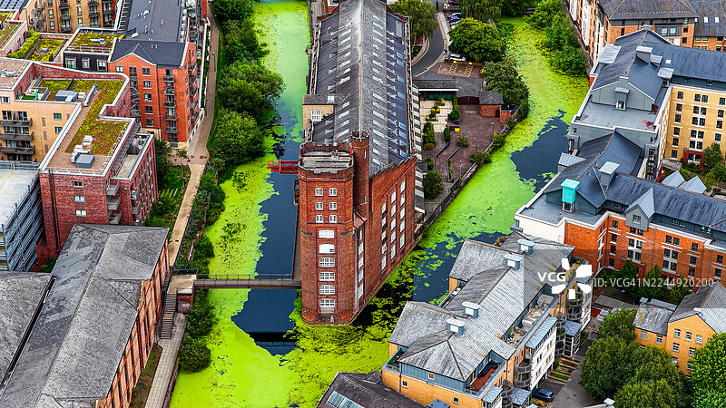 从空中俯瞰英国北部约克市历史悠久的红砖工业磨坊建筑，周围环绕着现代公寓和绿色的运河，体现了城市遗产与建筑的理念图片素材