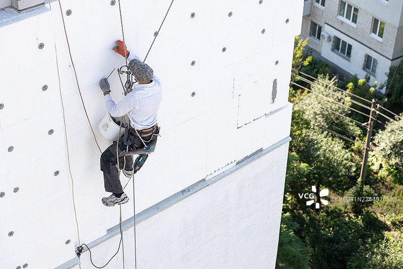 建筑工人用锚栓固定聚苯乙烯板，用于外墙保温。图片素材