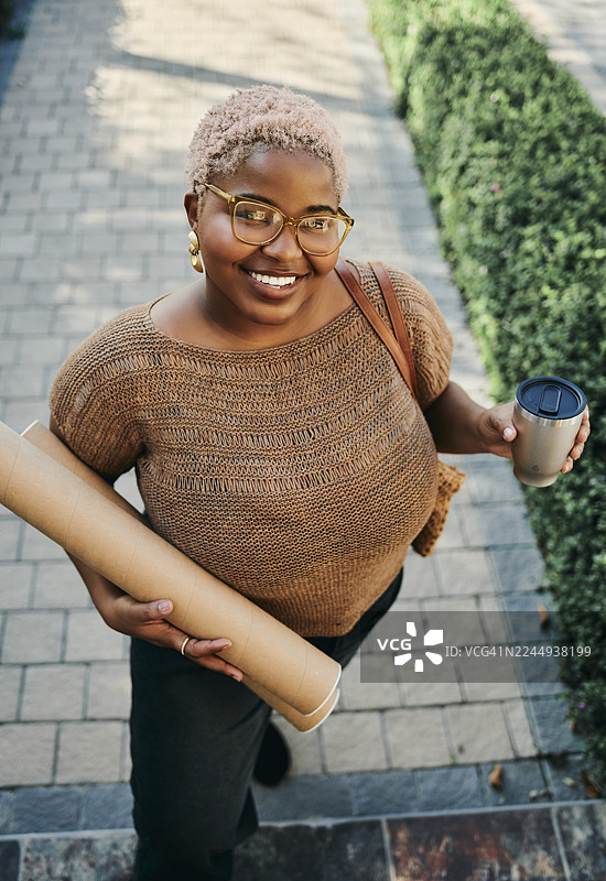 年轻的创意女性，穿着休闲装，在户外携带蓝图管和咖啡杯。图片素材