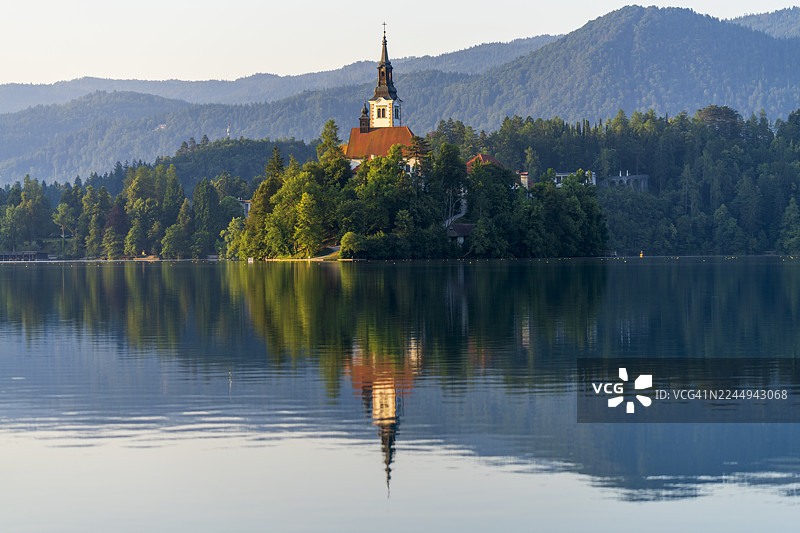 布莱德湖岛上宁静的教堂倒映在平静的水面上，背景是连绵的山脉图片素材