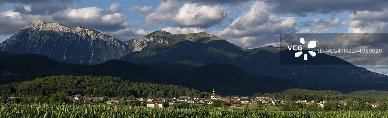 斯洛文尼亚的一个村庄坐落在绿色的田野和雄伟的朱利安阿尔卑斯山脉之间,靠近斯洛文尼亚的克兰伊。图片素材