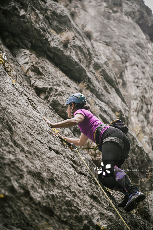 身穿紫色衬衫的女攀岩者在雨中利用绳索装备攀爬岩石峭壁图片素材