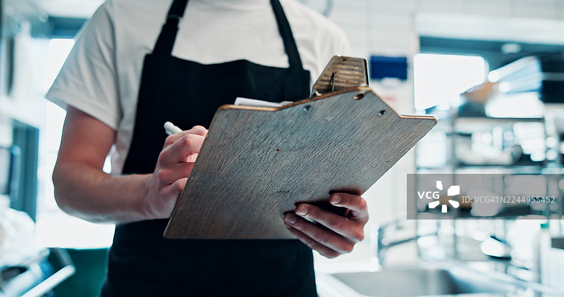 厨师在厨房里，手拿剪贴板记录，用于食品安全、卫生或库存管理。一名男子在餐厅里查看笔记和清单，用于质量控制、酒店业合规和法规。图片素材