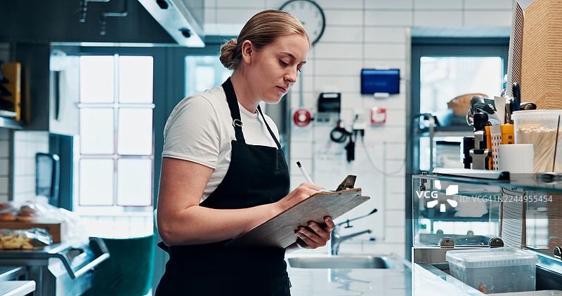 厨师在厨房检查食物或撰写清单，用于安全、卫生或库存管理。女性在餐厅手持笔记和剪贴板，进行质量控制、酒店业合规和规则检查。图片素材