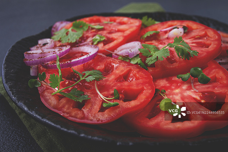 新鲜切片的番茄和红洋葱，用香草点缀，放在黑色盘子上，夏日沙拉，无人图片素材