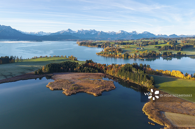 德国巴伐利亚州施瓦本地区奥斯阿尔高县福尔格湖附近伊拉施贝格湖的宽阔风景，平静的湖泊和色彩缤纷的树木，背景为阿尔卑斯山图片素材