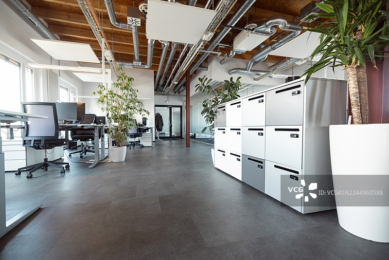 现代办公室内部，配有文件柜、工作站、电脑和少量绿植。图片素材