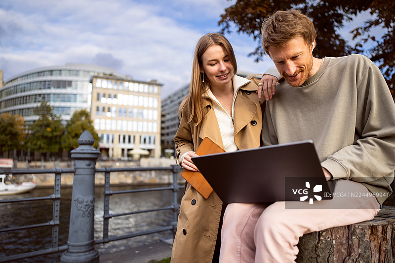 年轻情侣在柏林卡尔·李卜克内西桥上看着笔记本电脑，女子手中拿着平板电脑图片素材