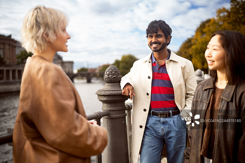 一群来自不同背景的年轻游客开心地在桥上聊天，背景是柏林大教堂。图片素材