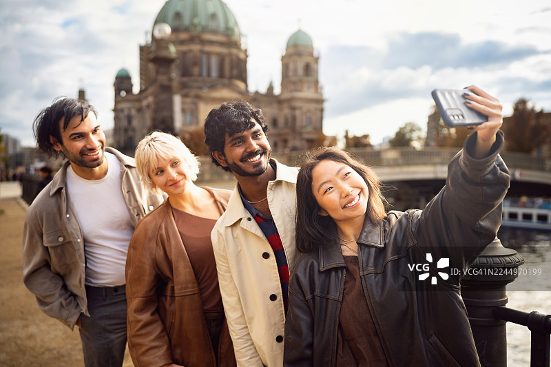一群来自不同背景的年轻游客在柏林施普雷河边，以柏林大教堂为背景，自拍留念图片素材