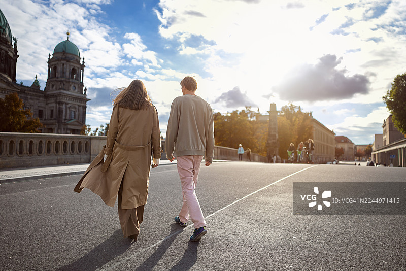 年轻情侣携手走过桥梁，背景是柏林大教堂的壮丽景色图片素材