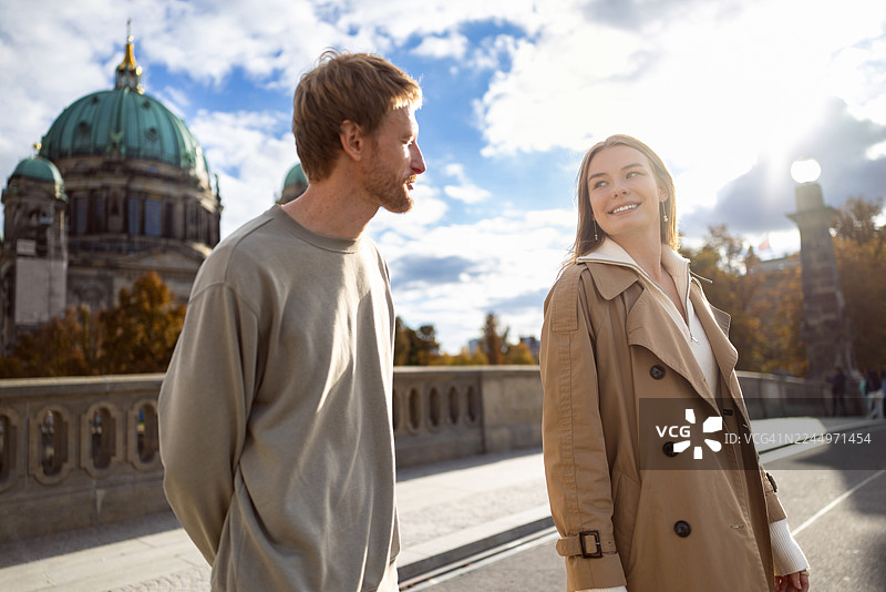 一对年轻的微笑情侣正走在桥上，背景是柏林大教堂的景色图片素材