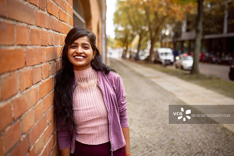 身穿紫色服装、靠在柏林砖墙上的年轻快乐印度女性肖像图片素材