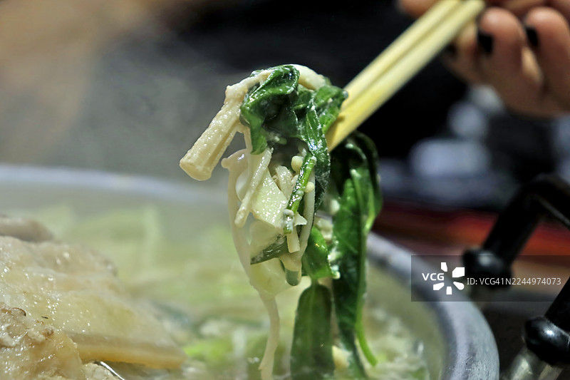 筷子从泰式烧烤或涮涮锅亚洲烤架的沸腾汤中捞起新鲜的绿菠菜和金针菇，重点是蒸腾的蔬菜图片素材